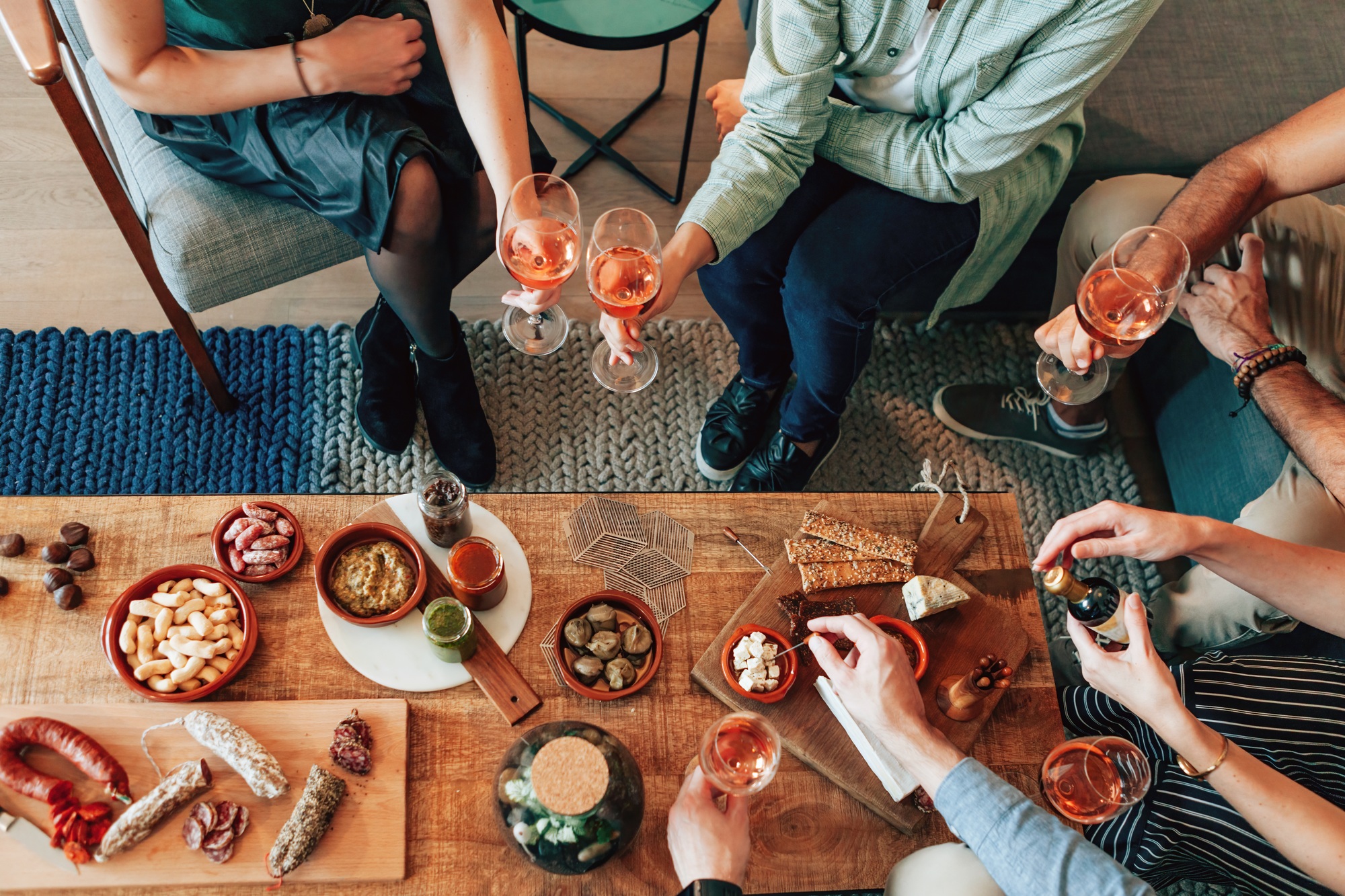 top view of unrecognizable people sitting around the living room table with food and wine